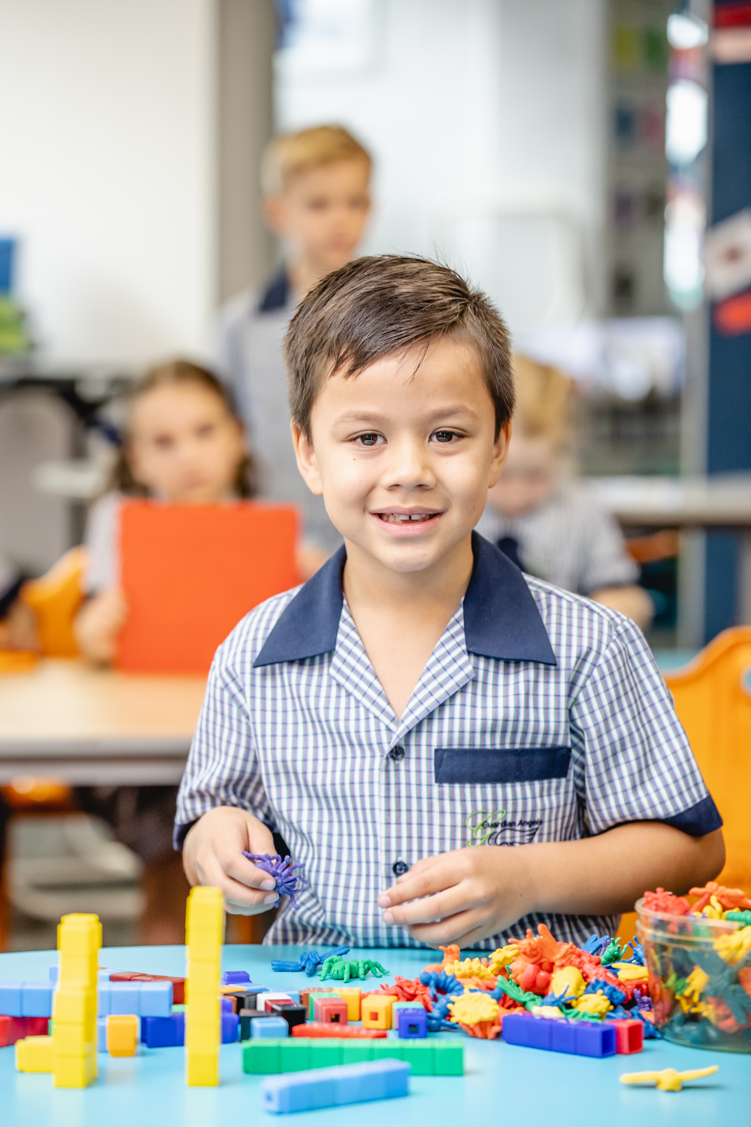 Student in a classroom using colourful building blocks, with other students in the background.