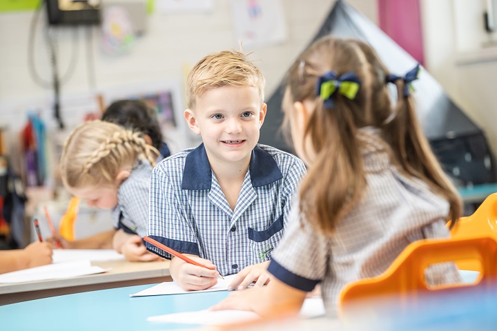 Students in a classroom working together at desks, writing on paper.