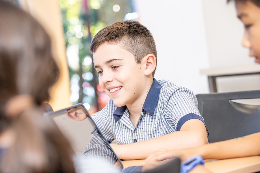 Student using a tablet in a classroom, with other students nearby.