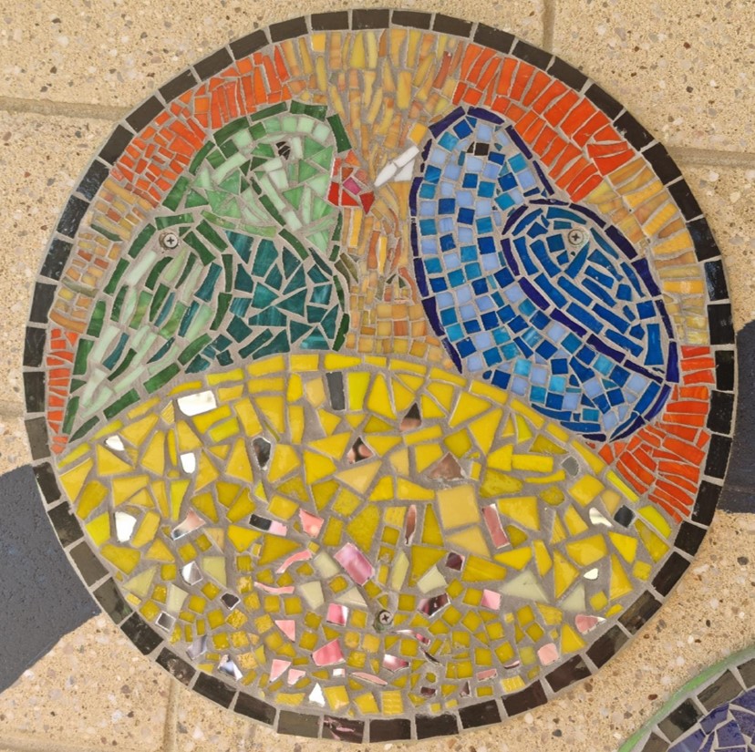 Circular mosaic artwork showing two birds perched facing each other above a yellow patterned background.